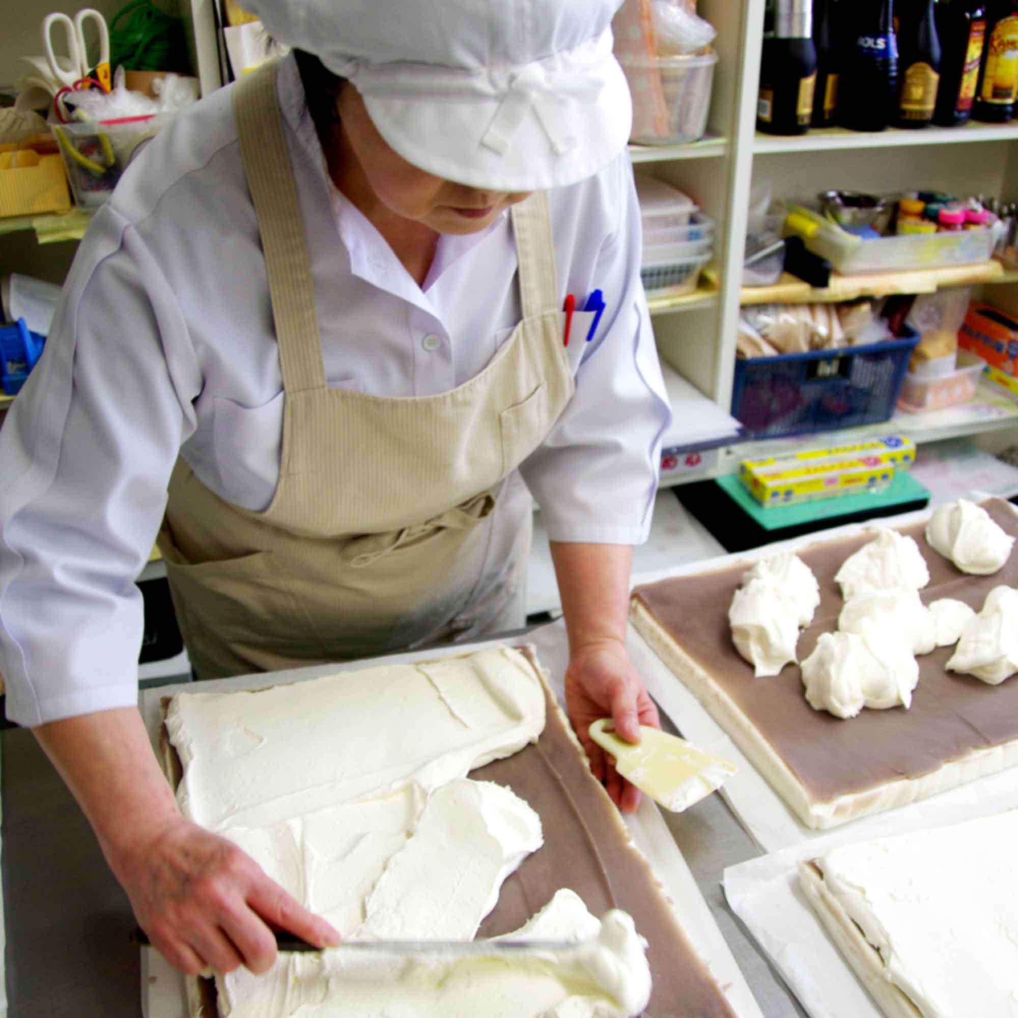 山形県アンテナショップおいしい山形　つくり手を訪ねて｜有限会社ぱんどら：スポンジの上に、あんこ、生クリームを順に重ね、厚さが均一になるように手早く伸ばしていきます。